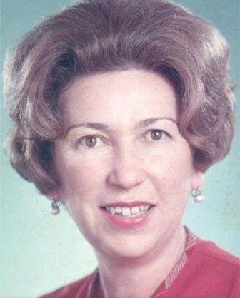 Woman with neatly styled brown hair smiles, wearing pearl earrings and a red top.