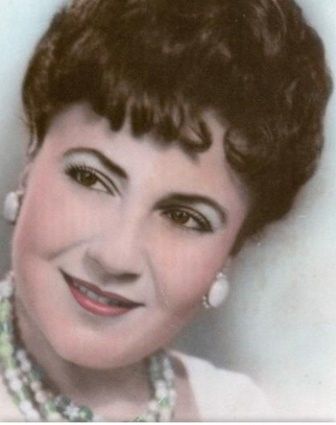 Woman with dark curly hair, smiling, wearing pearl earrings and necklace.