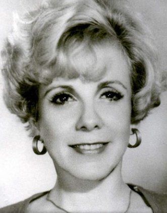 Woman with curled blonde hair smiles, wearing large hoop earrings.