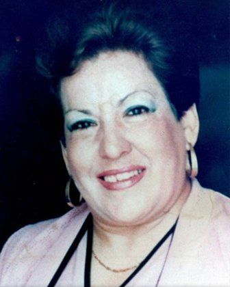 Woman smiling, wearing pink top, black strap, and hoop earrings.