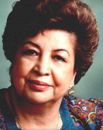 Woman with brown hair and light skin smiles, wearing a patterned top and gold earrings.