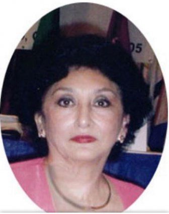Woman with dark hair and red lipstick, wearing a pink top and gold necklace.