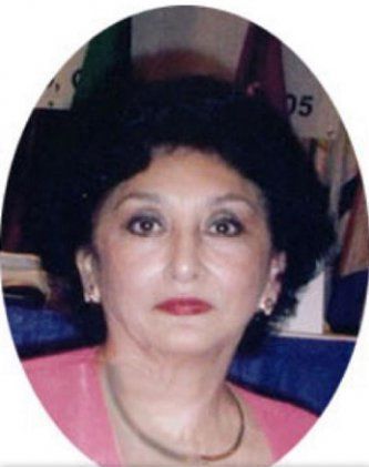 Woman with dark hair, red lipstick, and a pink top. She wears a necklace and earrings.