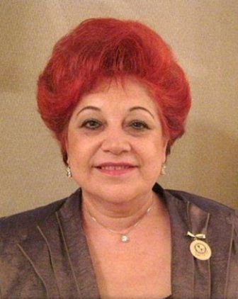 Woman with vibrant red hair, wearing a brown jacket, smiles at the camera, a pin on her lapel.