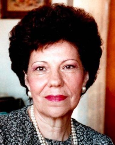 Woman with dark, curly hair and red lipstick, wearing pearl necklace and earrings.