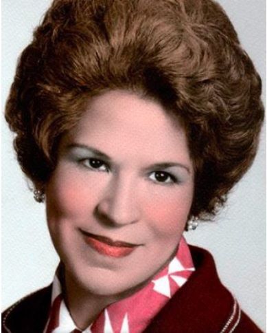 Woman with styled brown hair, wearing a dark red blazer and patterned scarf, smiling.