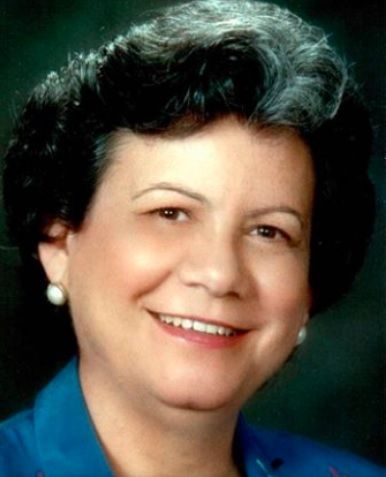 Woman smiling, wearing a blue top and pearl earrings, dark curly hair, studio shot.
