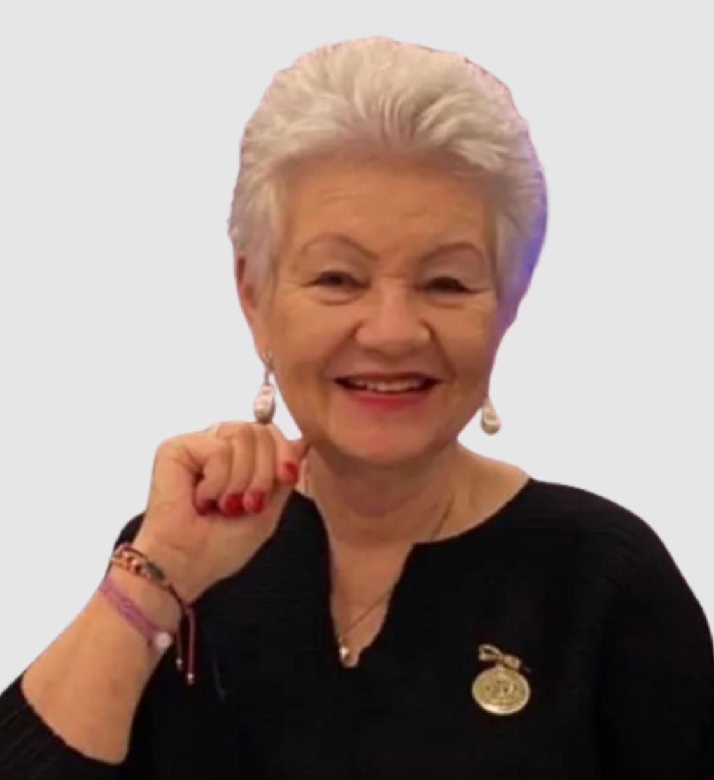Woman with white hair smiles, fist raised. Wearing black top, gold pendant, and dangling earrings.