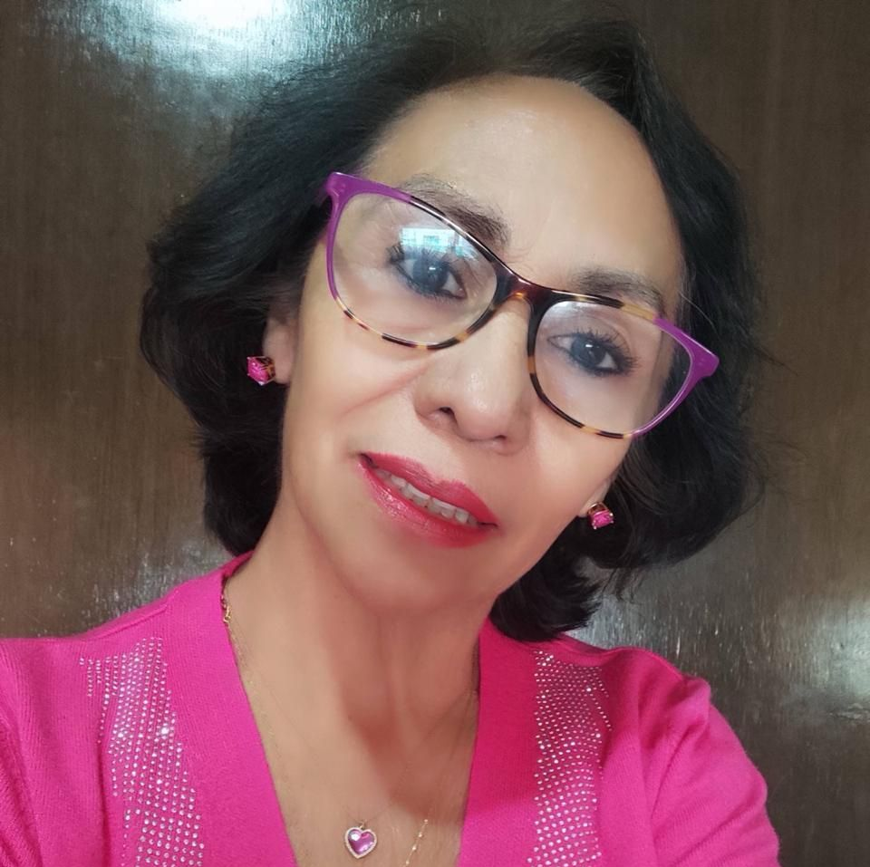 Woman wearing glasses and pink top smiles at the camera.