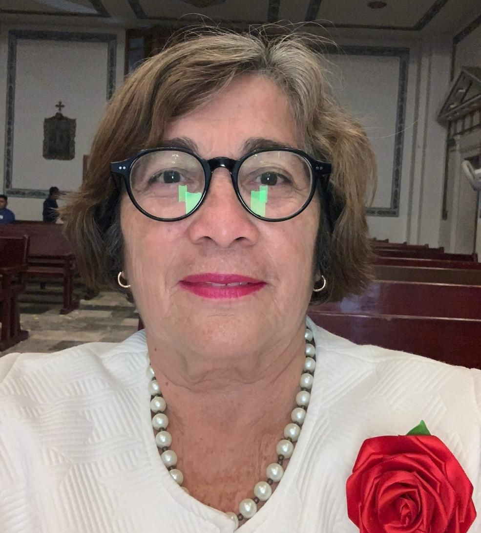 Woman wearing glasses, pearl necklace, and red rose pin, in a church.