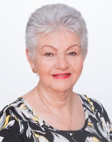 Woman with short, gray hair smiles, wearing gold earrings and a patterned top, against a white background.