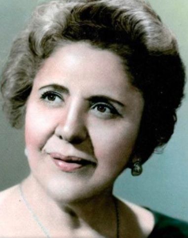 Woman with light-colored hair, wearing earrings, smiling slightly, posing for a portrait.