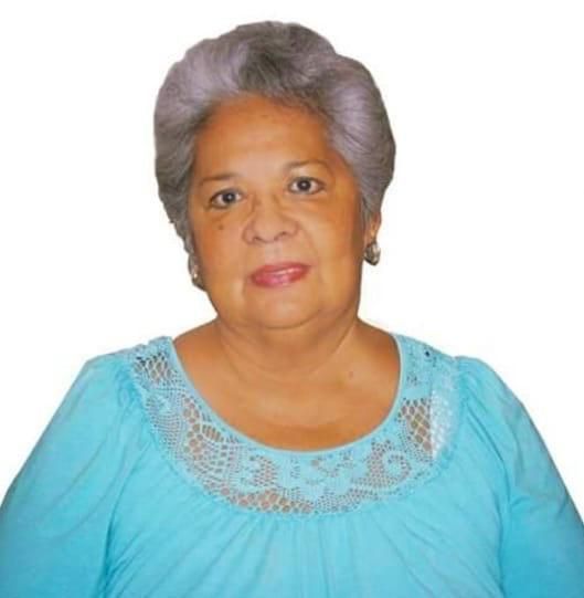 Woman with gray hair, wearing a blue shirt with lace neckline, smiles at the camera.