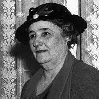 Woman in hat and blazer. Leaning slightly, looking toward the viewer. Black and white photo.