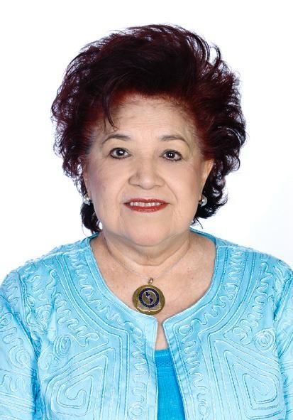 Woman with reddish-brown hair, wearing a blue textured top and a pendant, smiling at the camera.
