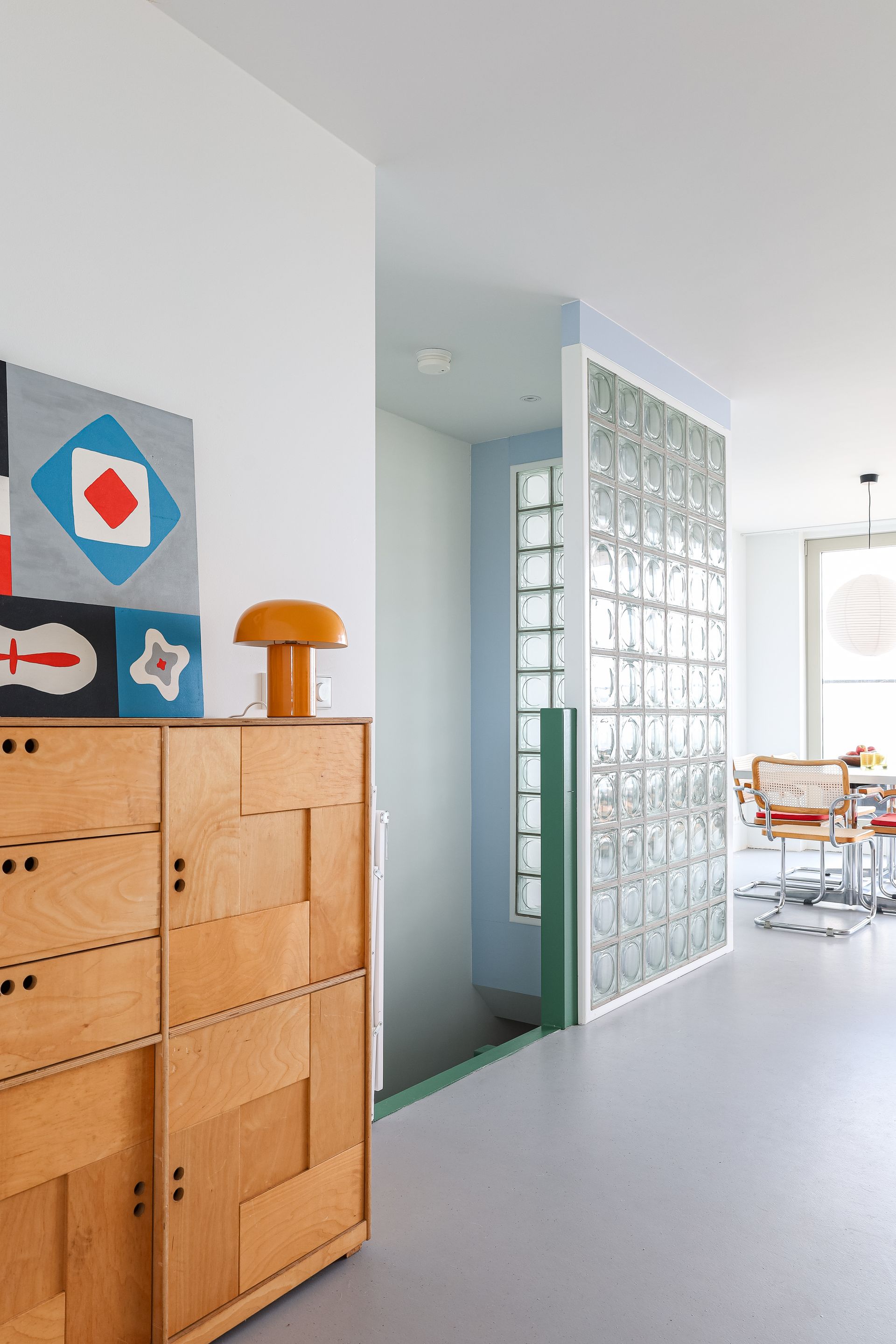 Houten kast met kunst en een lamp, naast een glazen bouwstenenwand en een trap. Glass blocks. Glazen blokken