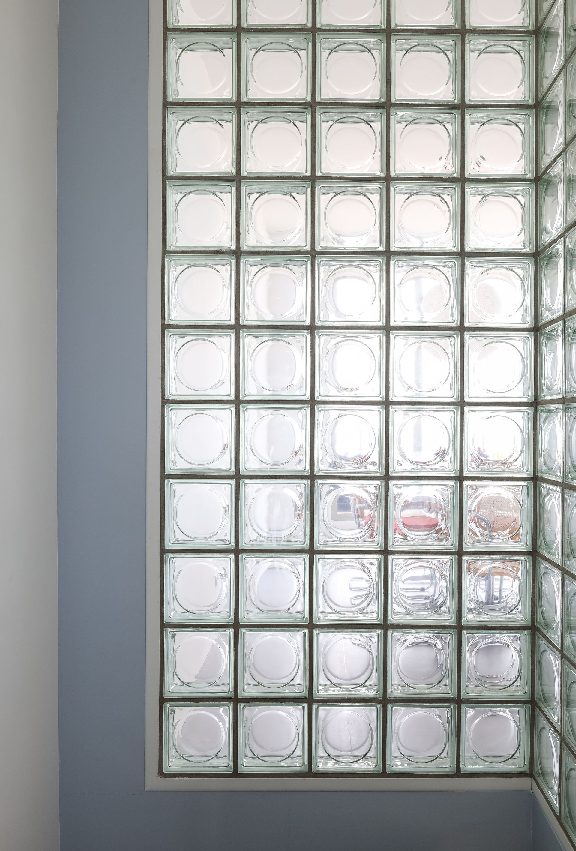 Een raam van glazen bouwstenen in een hoek, naast een blauwe muur. Glass blocks.