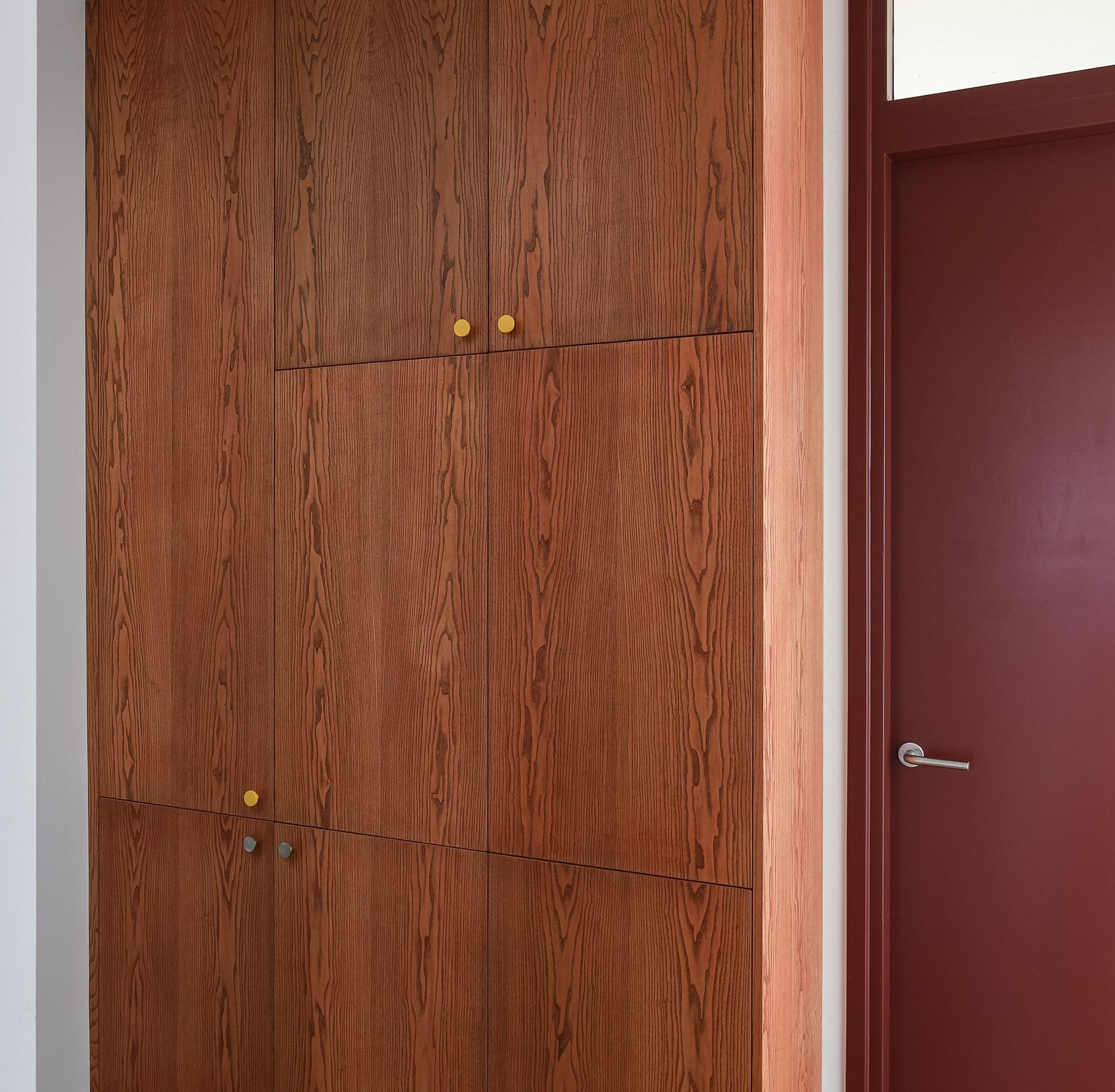 Houten maatwerkkast met gele knoppen, naast een bordeauxrode deur. Kleuradvies.