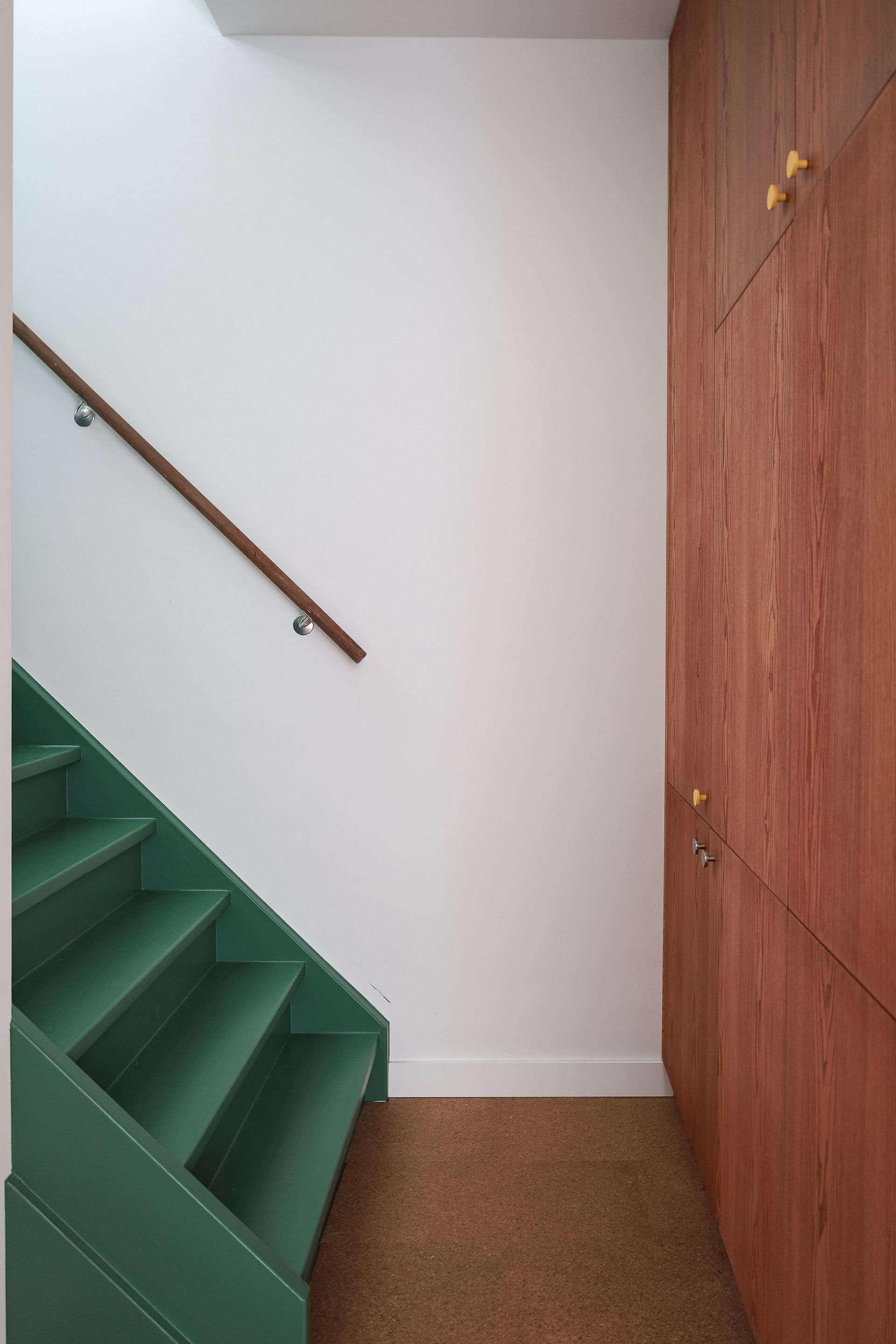 Groene trap met houten leuning tegen een witte muur, met een houten kast. Maatwerk.