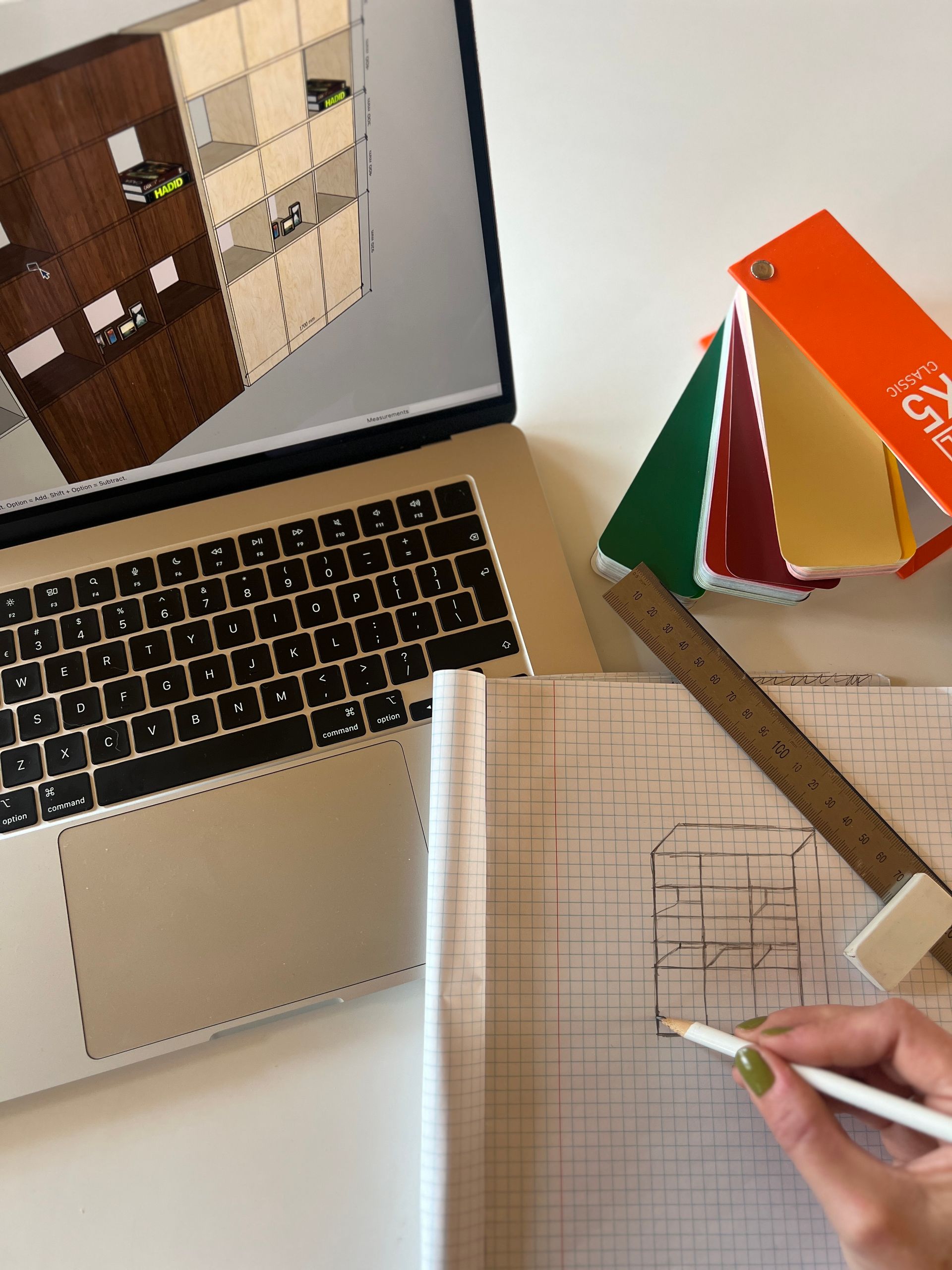 Een laptop waarop een 3D-ontwerp wordt weergegeven, een hand die een blauwdruk op ruitjespapier schetst.