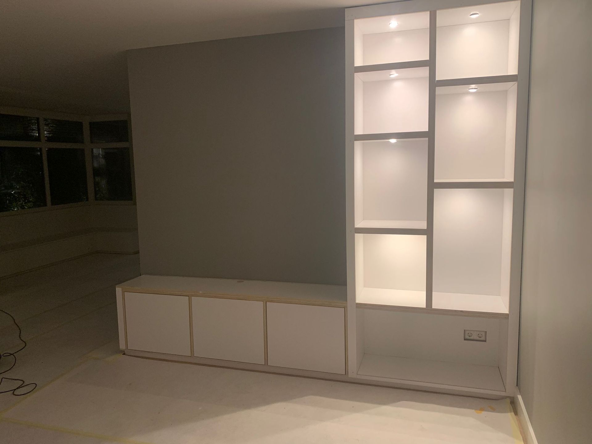 Witte ingebouwde wandkast met verlichte vakken naast een grijze muur en witte opbergkasten. Maatwerkadvies. Interieuradvies.