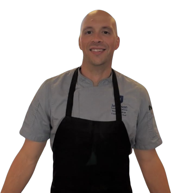 Chef in gray uniform and black apron, smiling, arms outstretched.