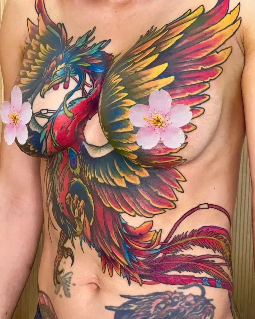 Colorful phoenix tattoo on a person's torso, with cherry blossom stickers over nipples.