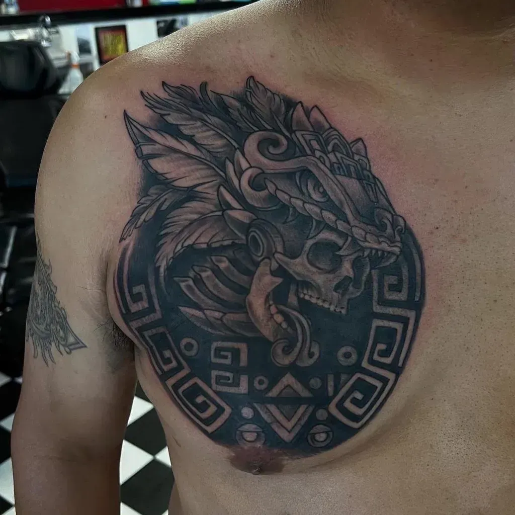 Tattoo of a skull with feathered headdress and geometric design on a person's chest.