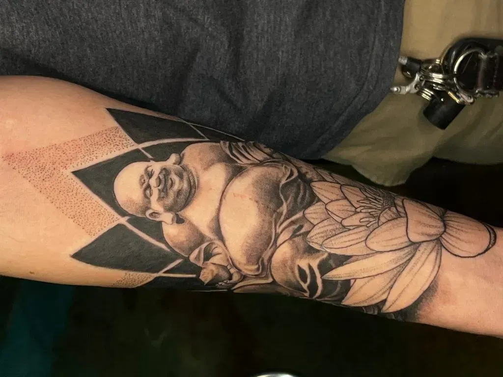 Tattoo of a reclining Buddha figure with a lotus flower and geometric shapes on an arm.