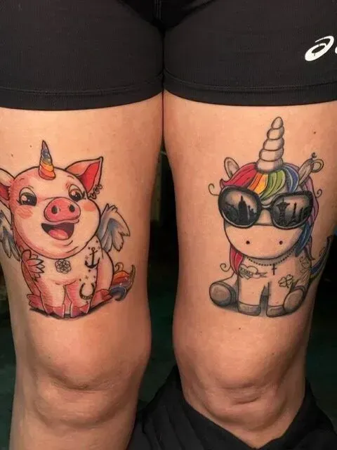 Tattoos of a pig with wings and a unicorn wearing sunglasses are on a person's knees.