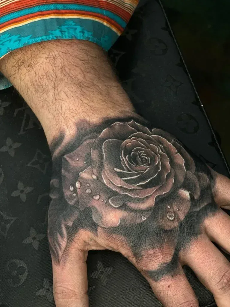 Hand with black and gray rose tattoo. Drops of water detail.
