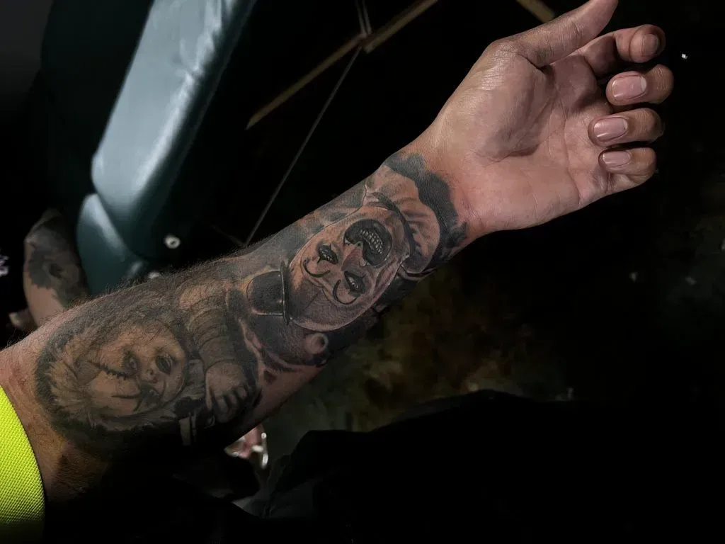 Arm with a large tattoo of Chucky doll on the forearm.