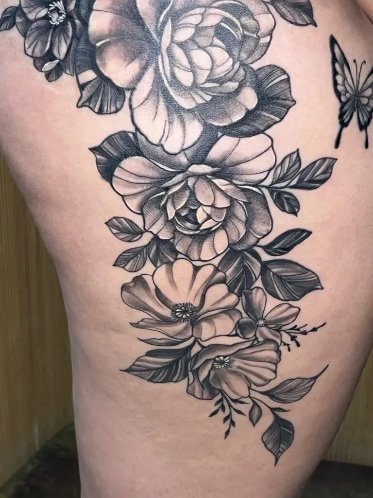Floral tattoo in black and gray on a person's side, with a butterfly on top.