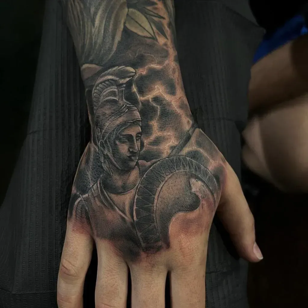Tattoo of a helmeted figure, possibly Athena, on the back of a hand, with a shield and lightning background.