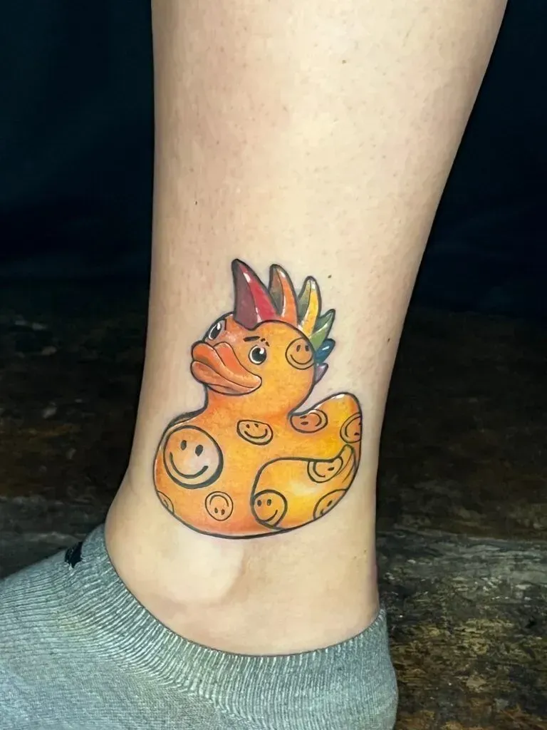Colorful rubber duck tattoo with smiley faces on ankle.