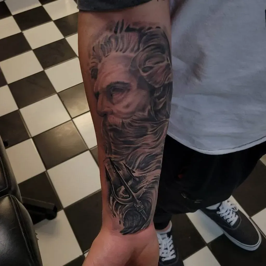 Tattoo of a bearded man with a stern expression and trident on a forearm.