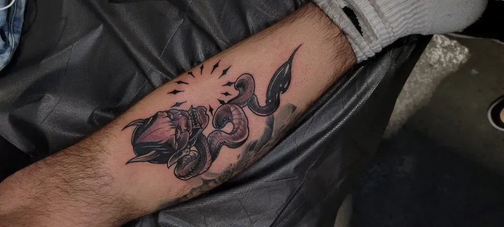 Tattoo on a forearm depicting a sun and a figure. The skin tone is light.