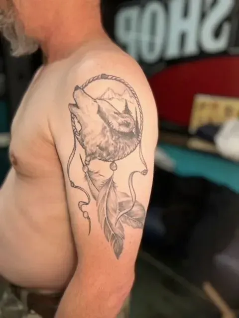 Tattoo of a howling wolf within a dreamcatcher on a person's upper arm.
