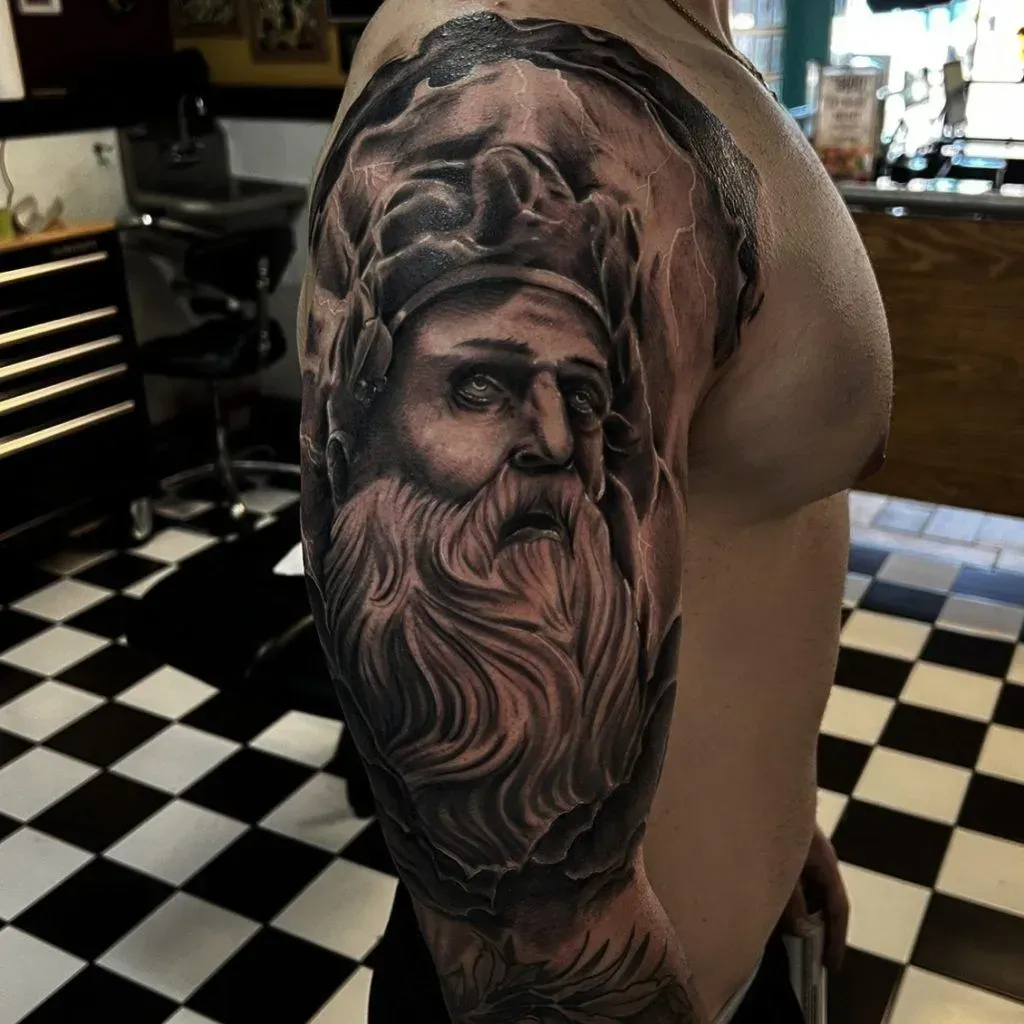 Black and gray tattoo of a bearded man on a person's upper arm. Checkerboard floor in the background.