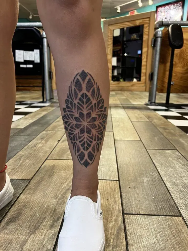 Leg with a symmetrical black floral tattoo, wearing a white shoe, indoors with wood flooring.