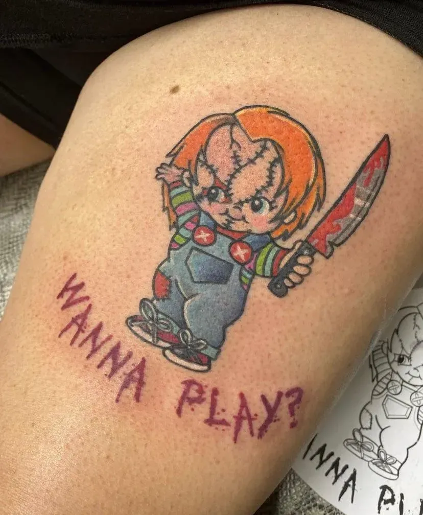 Chucky tattoo on leg, holding knife, with text