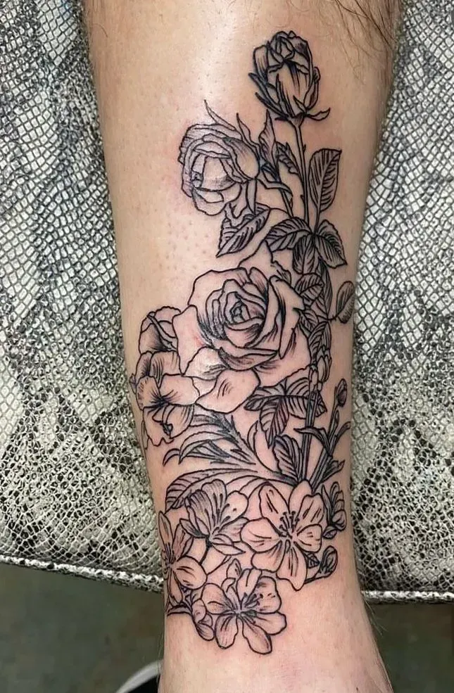 Black floral tattoo on skin, featuring roses and other flowers.