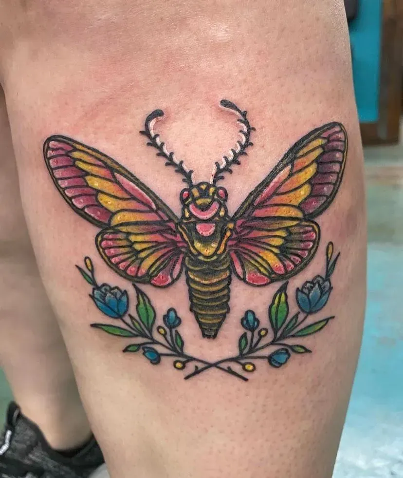 Colorful cicada tattoo on a leg, with floral accents.