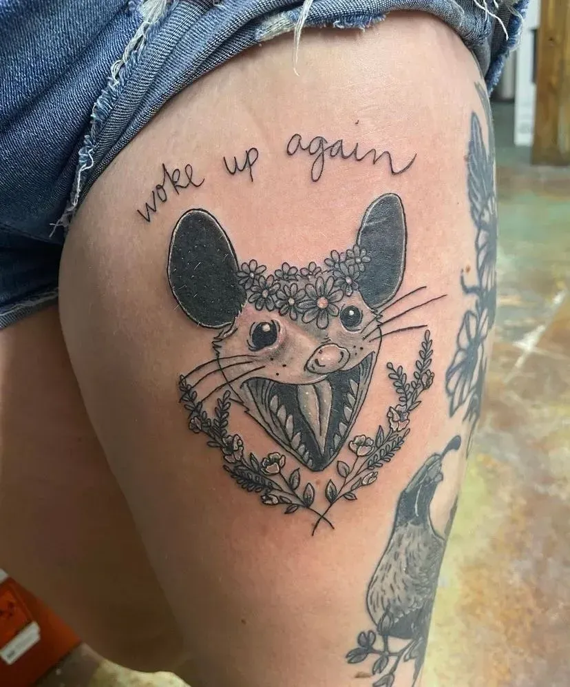 Tattoo of a mouse with a floral crown, open mouth, and text