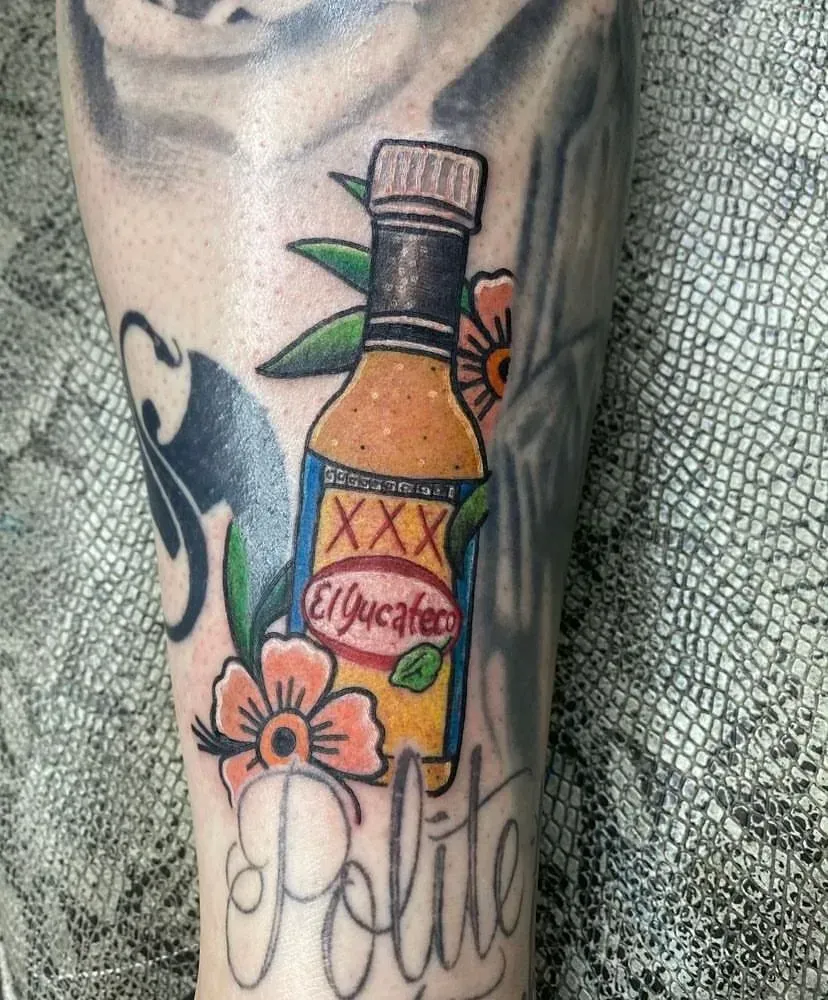 Tattoo of an El Yucateco hot sauce bottle with flowers, on a leg, surrounded by other tattoos, including the word