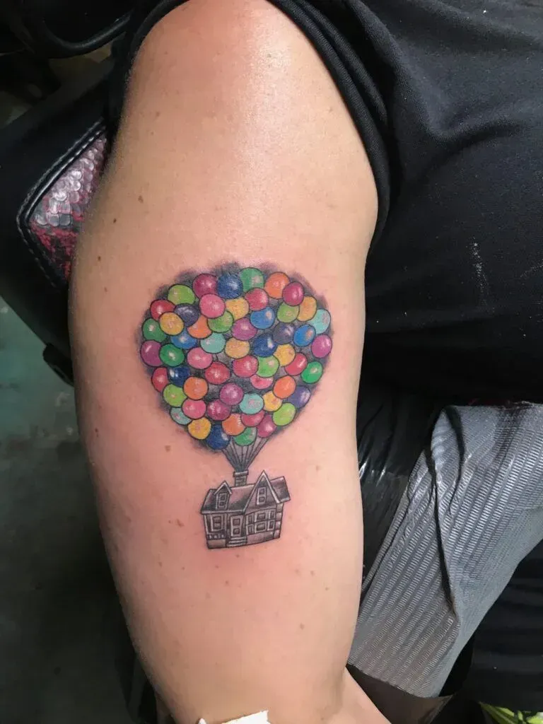 Tattoo of a house floating with colorful balloons on an arm.