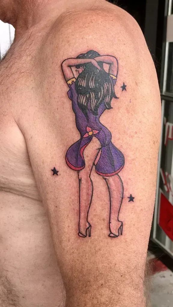 Tattoo of a woman in a purple dress, arms raised behind her head, on a man's arm, with stars.