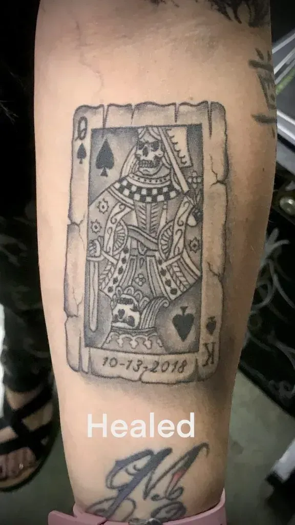 Tattoo of a Queen of Spades card with a skeleton design, dated 10-13-2018, on a person's arm.