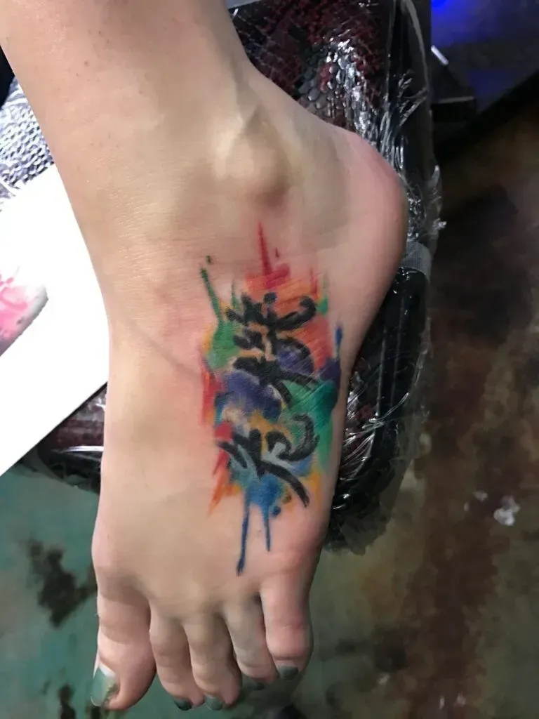 Foot tattoo: Chinese characters with colorful watercolor splashes.