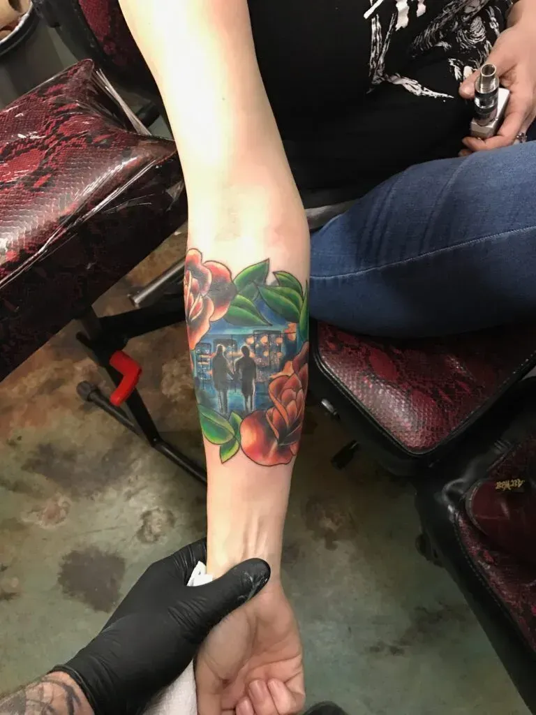 Arm with colorful tattoo of flowers and figures. Person's arm being held by gloved hand.